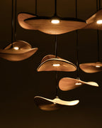 Close view of Clérachic wooden leaf pendants glowing against a dark background, each with a small round light.