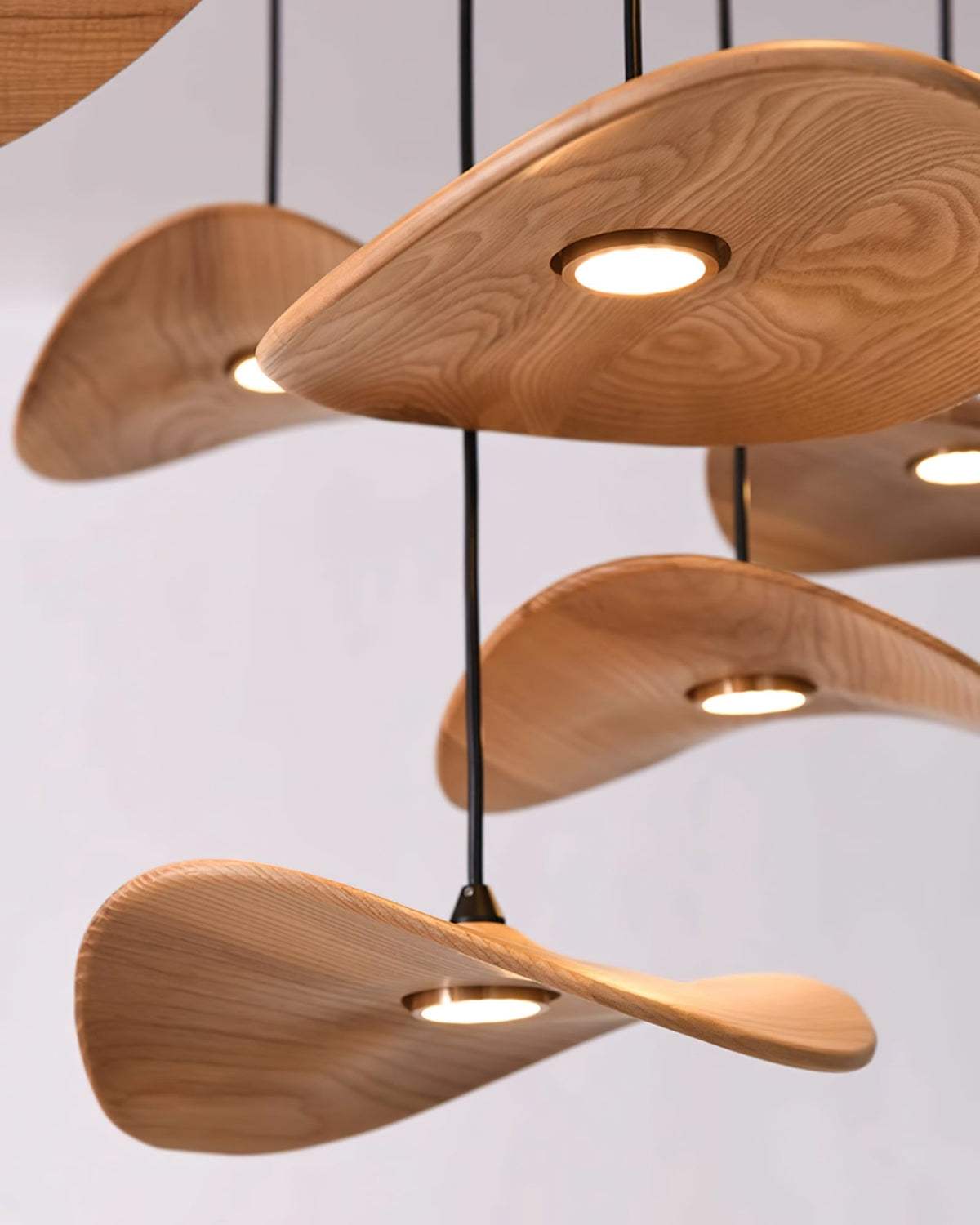 Close view of the pale ash grain on Clérachic leaf pendants, each with a small round brass-rimmed light underneath.
