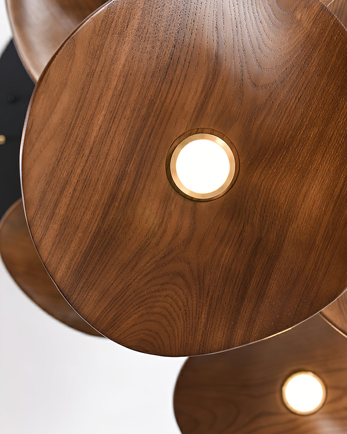 Close-up of a walnut-colour Clérachic leaf pendant with a round brass-rimmed light, and dark grain across the surface.