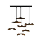 Eight Clérachic leaf pendants in dark walnut colour hung at varied heights from a black canopy, on white.