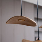 Close view of a light wood Clérachic leaf pendant with a round brass-rimmed light, against a soft grey wall.