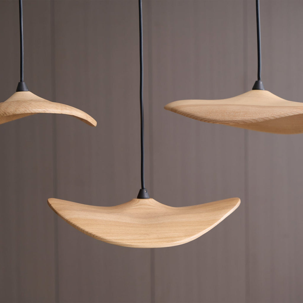 Looking up at Clérachic wooden leaf pendants with curved, upturned edges, against a grey-brown wall.
