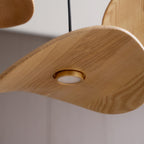 Close-up of the ash grain and the small brass-rimmed round light beneath a Clérachic leaf pendant.