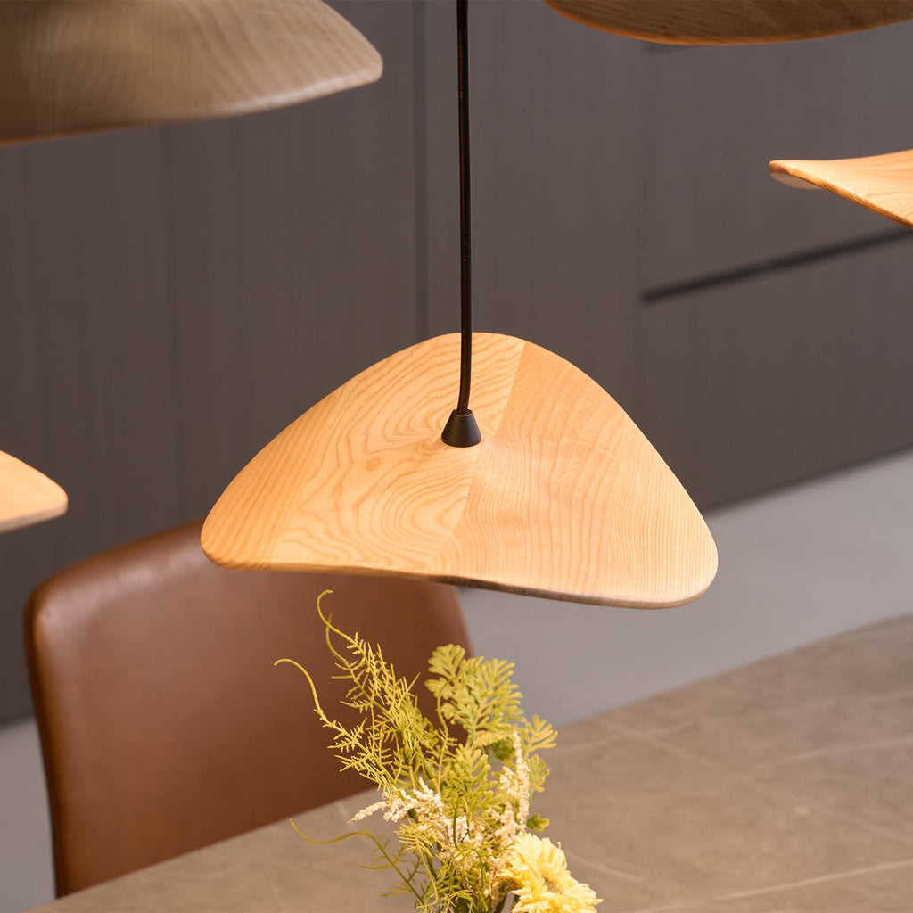 Light wood Clérachic leaf pendant lit warm above a brown leather chair, with a sprig of green foliage nearby.