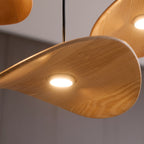 Close view of the curved underside of a Clérachic wooden leaf pendant, with its small round light switched on.