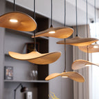 Clérachic wooden leaf pendants lit at different heights in a dining room, with shelves and curtains behind.