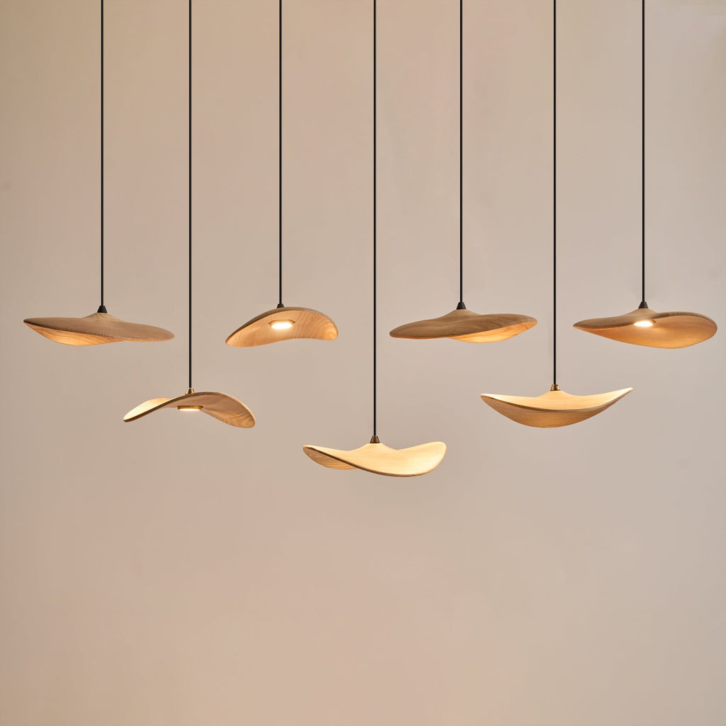 Seven Clérachic leaf pendants lit warm at staggered heights against a pale wall, with soft light on their undersides.