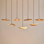 Seven Clérachic leaf pendants lit warm at staggered heights against a pale wall, with soft light on their undersides.