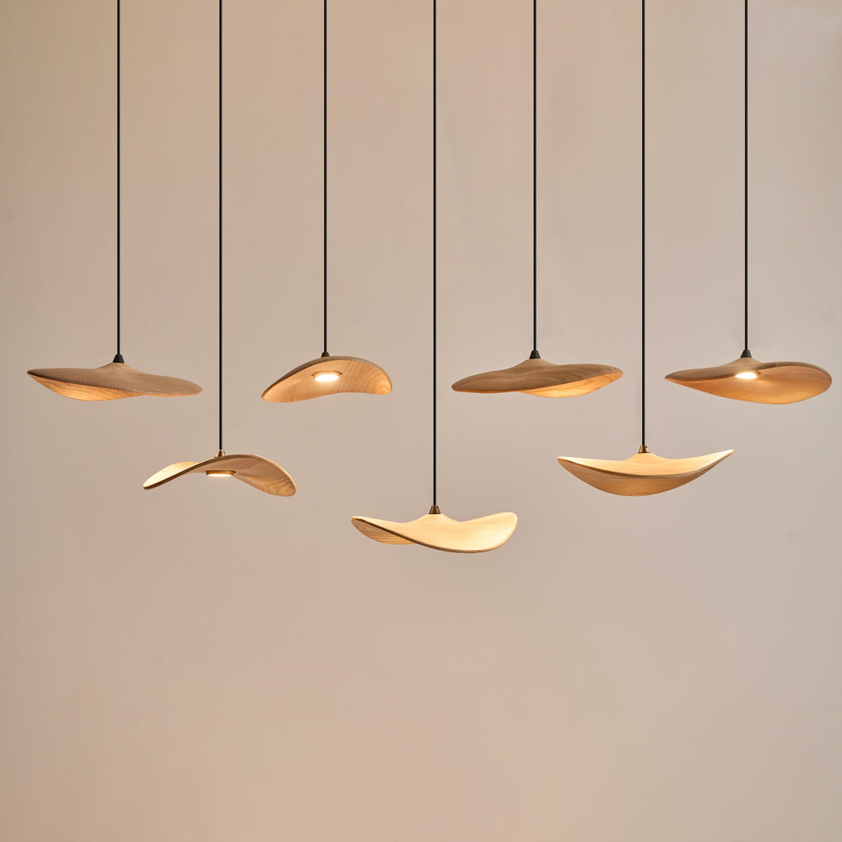 Seven Clérachic leaf pendants lit warm at staggered heights against a pale wall, with soft light on their undersides.