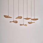 Clérachic wooden leaf pendants hung unlit at varied heights against a plain white wall, showing their wavy edges.