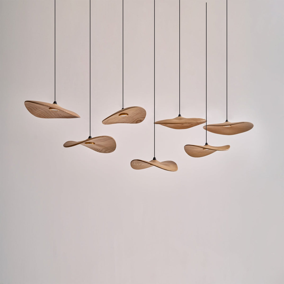 Clérachic wooden leaf pendants hung unlit at varied heights against a plain white wall, showing their wavy edges.