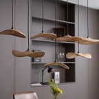 Clérachic wooden leaf pendants at several heights in front of a shelving unit with a lamp, books and glassware.