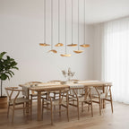 Seven small Clérachic leaf pendants over a light oak dining table with Wishbone-style chairs and a tall plant.