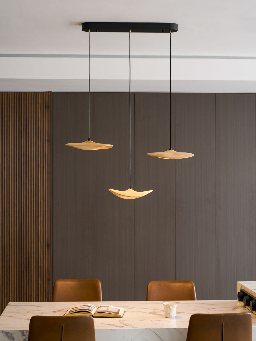 Three Clérachic leaf pendants on a black oval canopy over a marble island with leather stools and an open book.