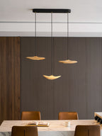 Three Clérachic leaf pendants on a black oval canopy over a marble island with leather stools and an open book.