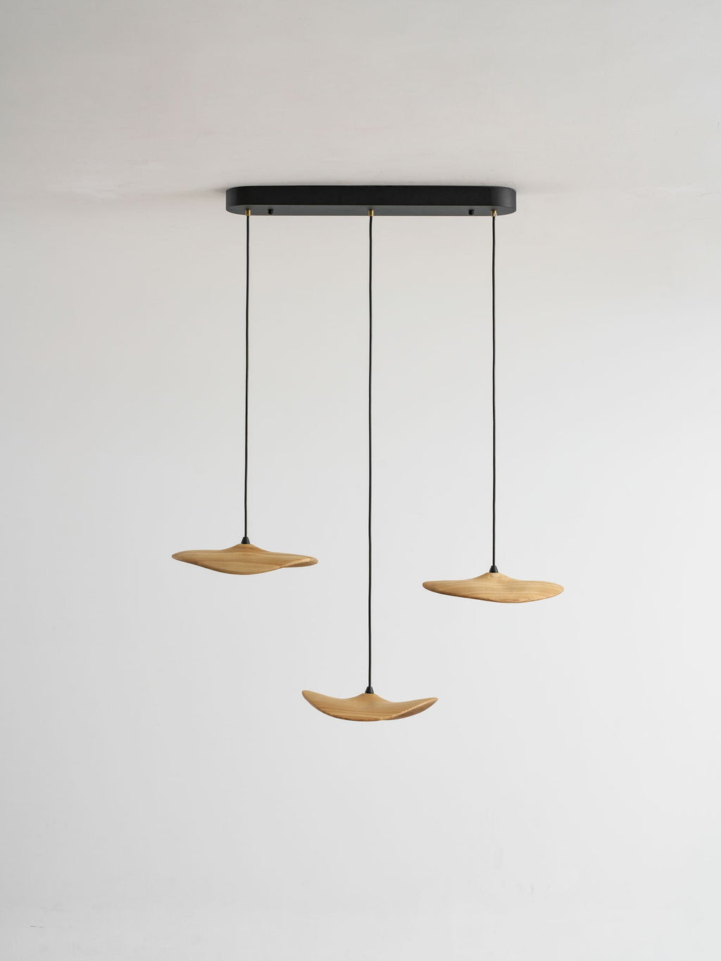 Three Clérachic wooden leaf pendants on a black oval canopy, hung at different heights against a plain grey wall.