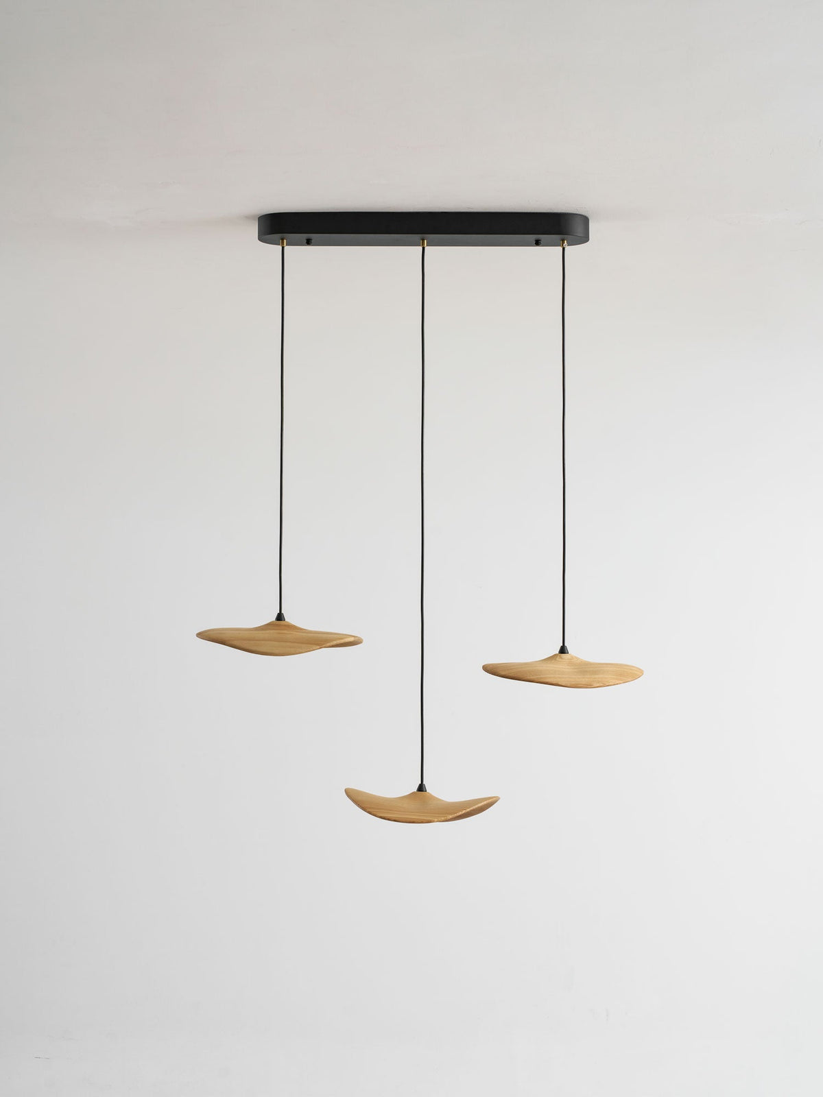 Three Clérachic wooden leaf pendants on a black oval canopy, hung at different heights against a plain grey wall.