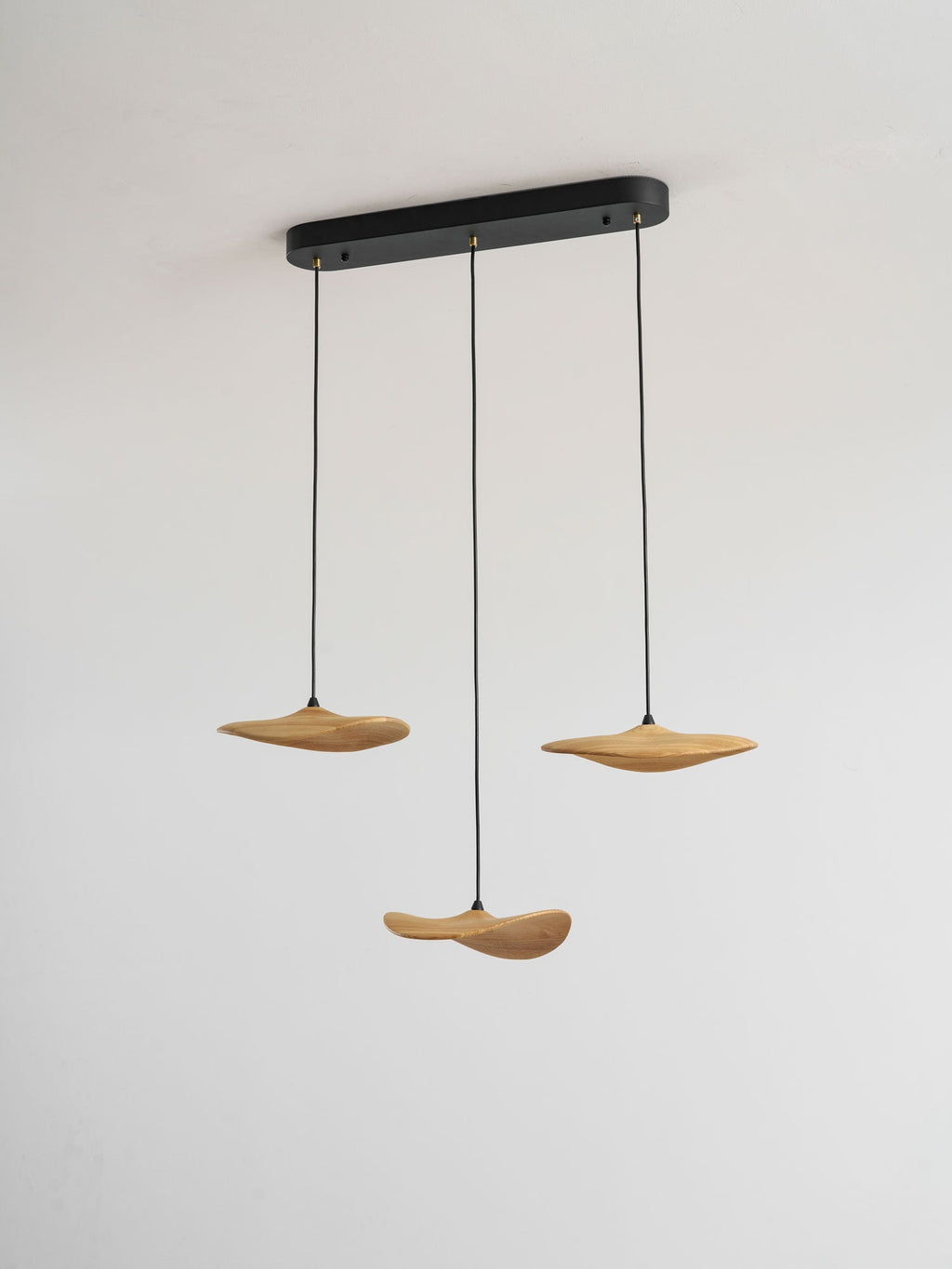 Three Clérachic light wood leaf pendants hung from a slim black oval canopy, against a plain pale wall.
