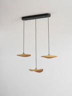 Three Clérachic light wood leaf pendants hung from a slim black oval canopy, against a plain pale wall.