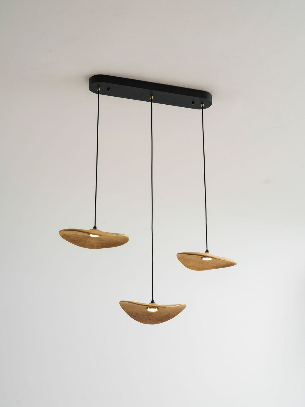 Three lit Clérachic leaf pendants hung from a black oval canopy against a light wall, with a warm glow beneath each.