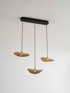 Three lit Clérachic leaf pendants hung from a black oval canopy against a light wall, with a warm glow beneath each.