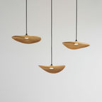 Three Clérachic wooden leaf pendants lit warm, hanging at different heights from long black cables.