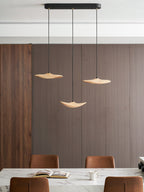 Three Clérachic leaf pendants over a marble island with an open book, a mug and leather chairs, before a ribbed wall.