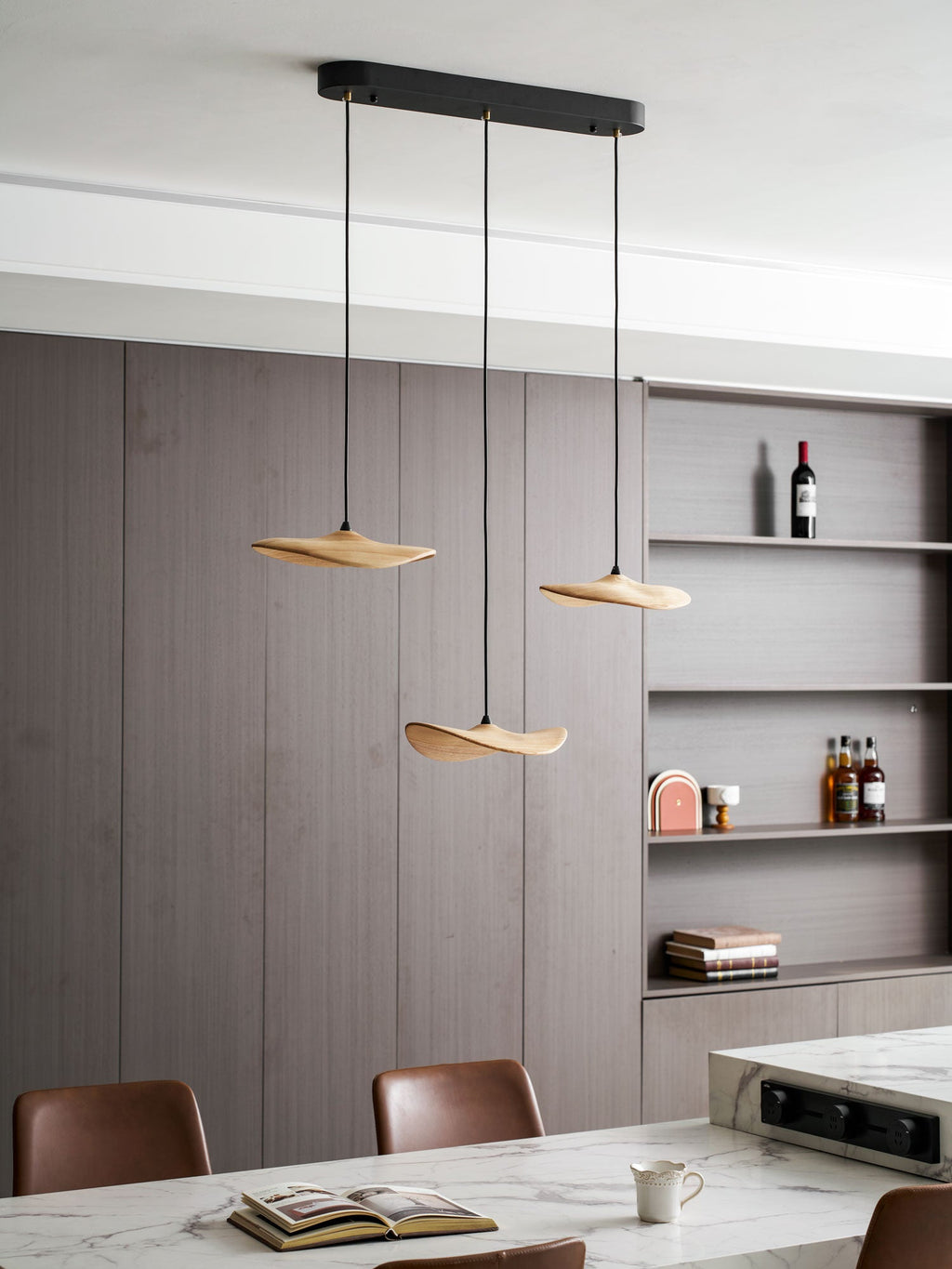 Clérachic leaf pendants with a black oval canopy over a marble counter, with shelves holding bottles and books behind.