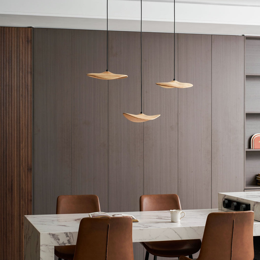 Three Clérachic wooden leaf pendants above a marble table with leather chairs and a wood slat panel at the left.
