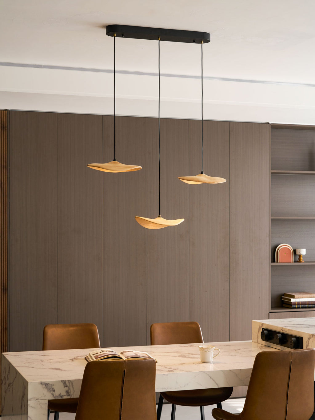 Three Clérachic leaf pendants lit in a dining room with grey-brown panelling, a marble table and tan leather chairs.