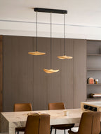 Three Clérachic leaf pendants lit in a dining room with grey-brown panelling, a marble table and tan leather chairs.