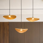 Three lit Clérachic wooden leaf pendants close up, warm light glowing from each, with wood panelling behind.