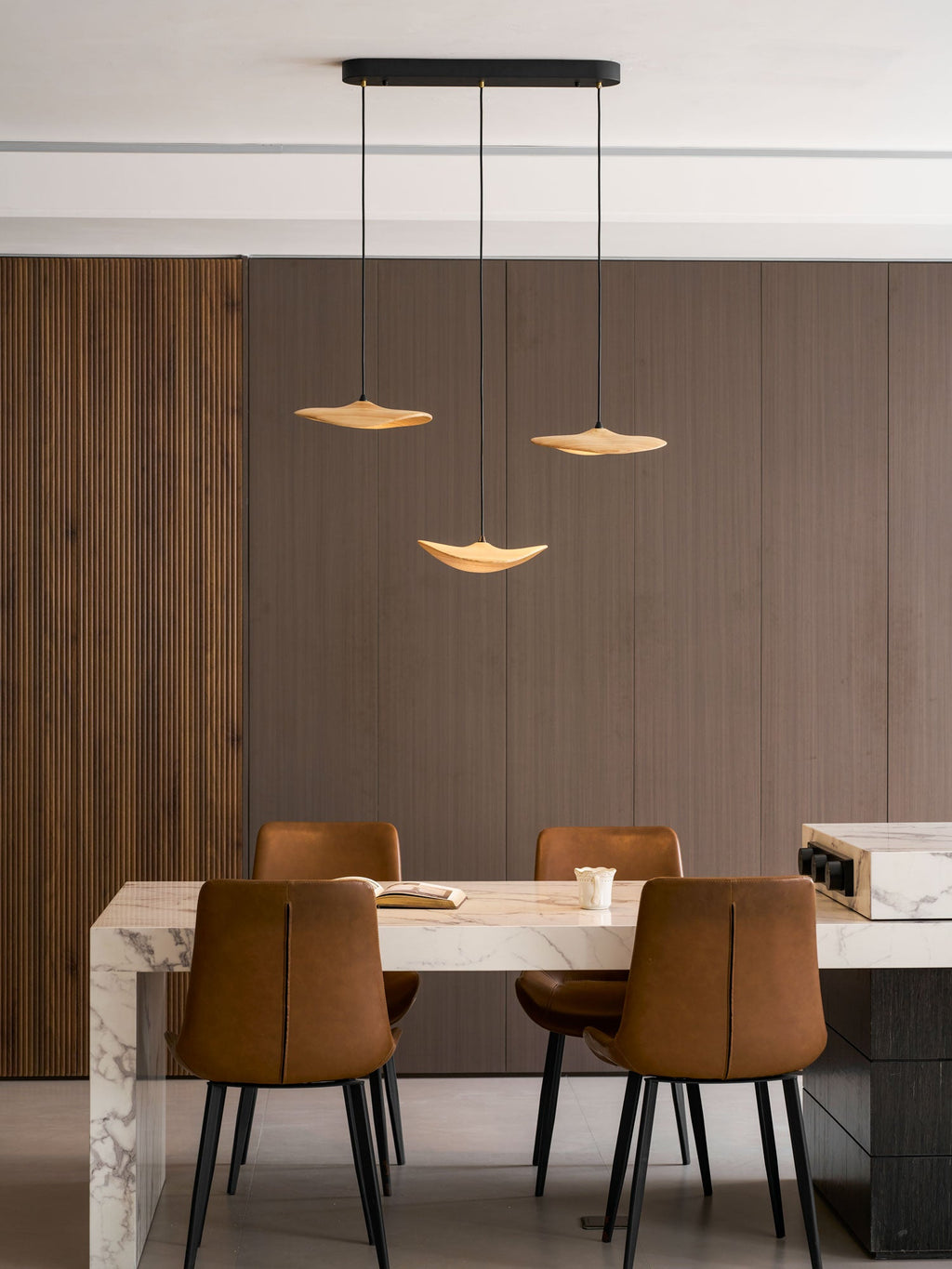 Three Clérachic leaf pendants hung over a marble-edged table with leather chairs, against dark wood panelling.