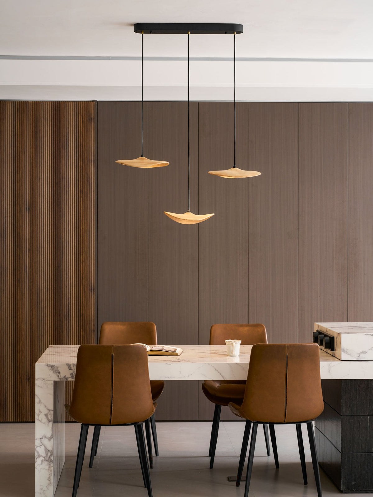 Three Clérachic leaf pendants hung over a marble-edged table with leather chairs, against dark wood panelling.