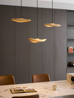 Close view of three lit Clérachic leaf pendants above a marble table with an open book and a mug.