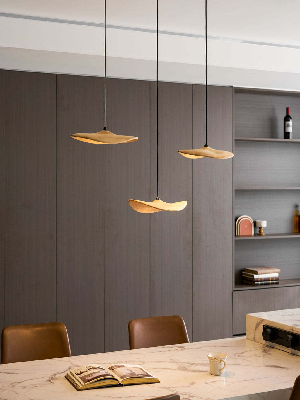 Clérachic leaf pendants lit above a marble table, with an open book, a cup and a shelf unit with a wine bottle.