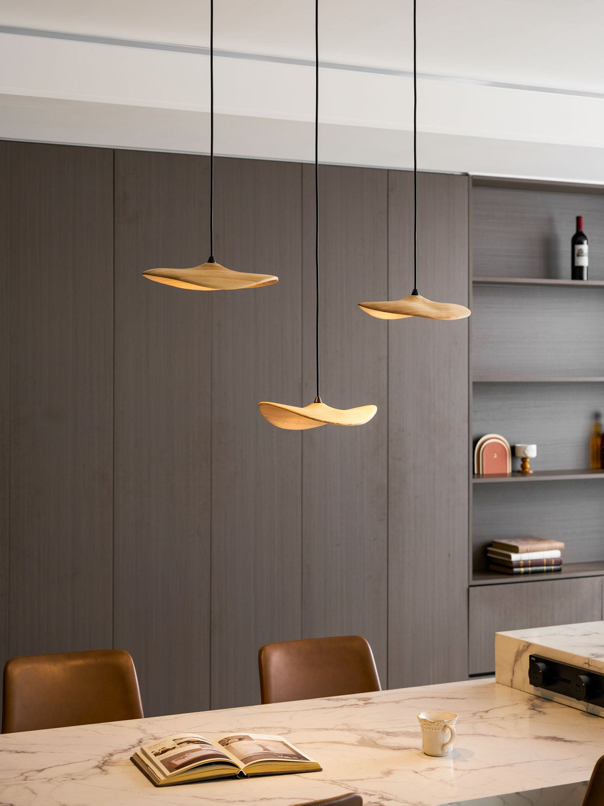 Clérachic leaf pendants lit above a marble table, with an open book, a cup and a shelf unit with a wine bottle.