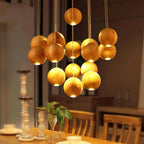 A Clérachic pendant of glowing wood spheres at varied heights over a dining table, with candlesticks and wooden chairs in the warm room below.
