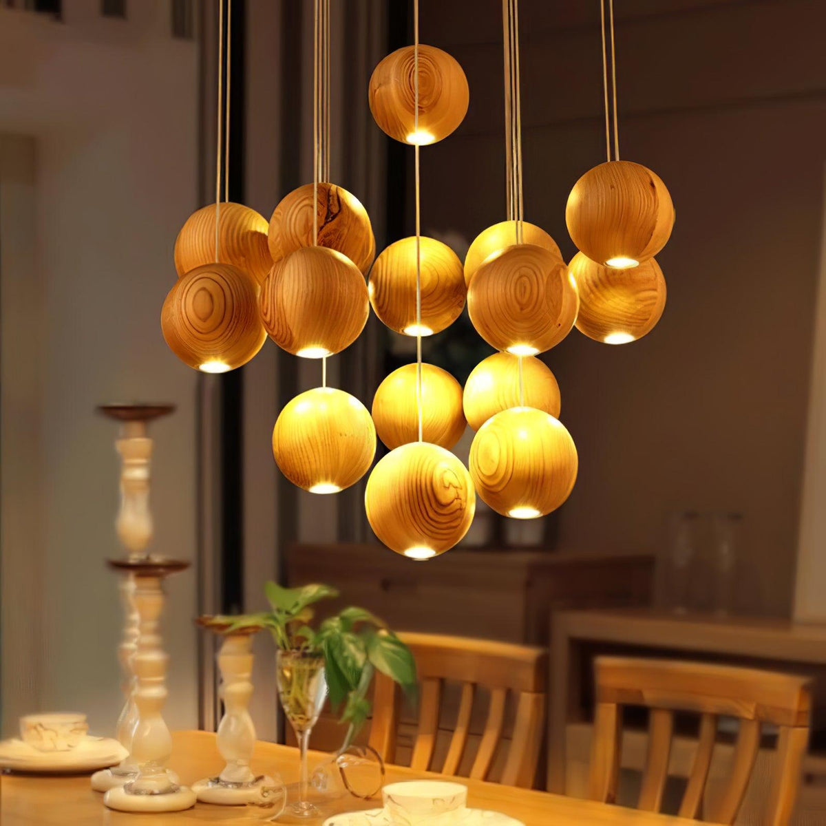 A Clérachic pendant of glowing wood spheres at varied heights over a dining table, with candlesticks and wooden chairs in the warm room below.