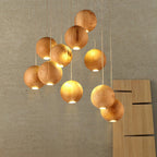 A Clérachic pendant light of lit wood spheres against a concrete-look wall, each with a warm glow from a small opening at its base.