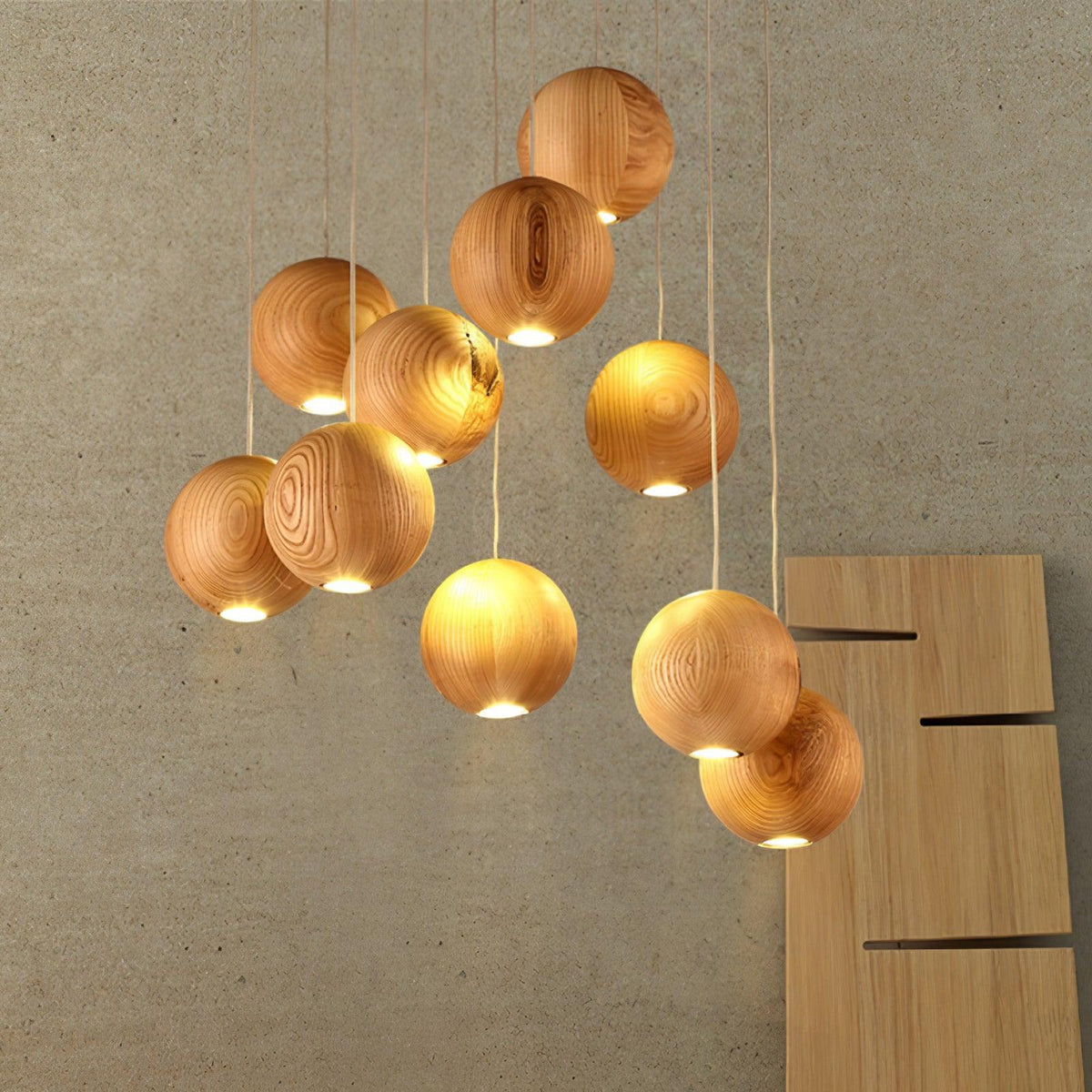 A Clérachic pendant light of lit wood spheres against a concrete-look wall, each with a warm glow from a small opening at its base.