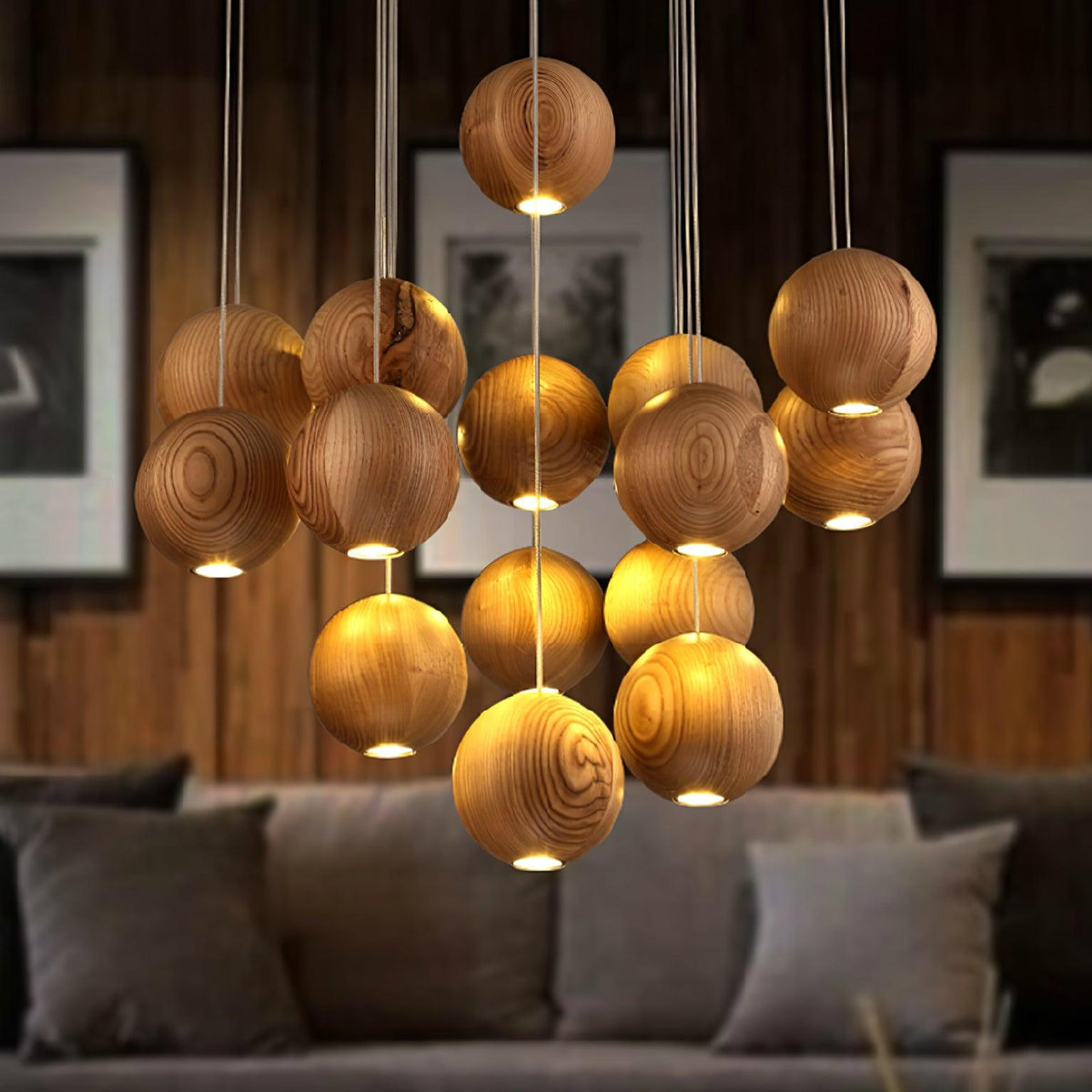A Clérachic wood-sphere pendant glowing warm over a grey sofa, with framed monochrome prints and a dark timber wall behind.