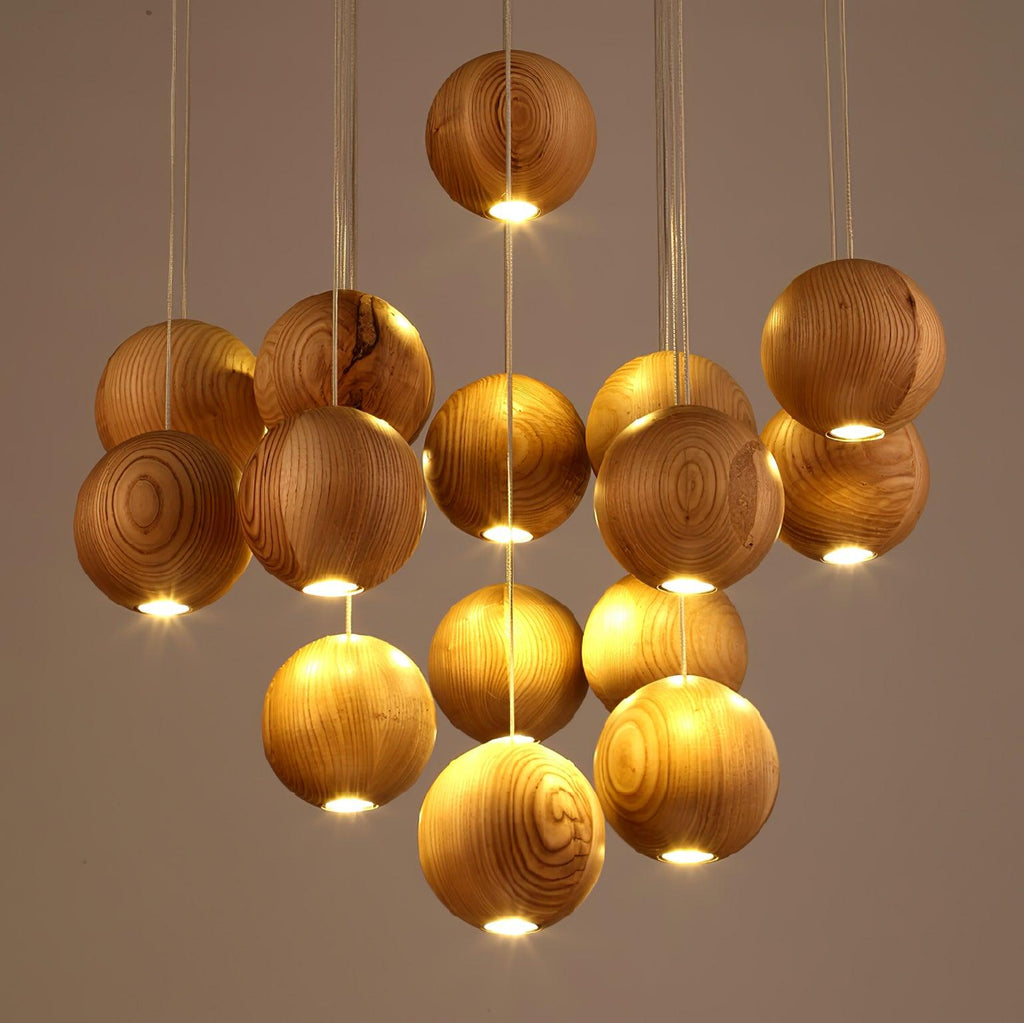 Close view of lit wood spheres on this Clérachic pendant, each with a warm glow from its base, against a soft taupe wall.