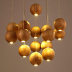 Close view of lit wood spheres on this Clérachic pendant, each with a warm glow from its base, against a soft taupe wall.