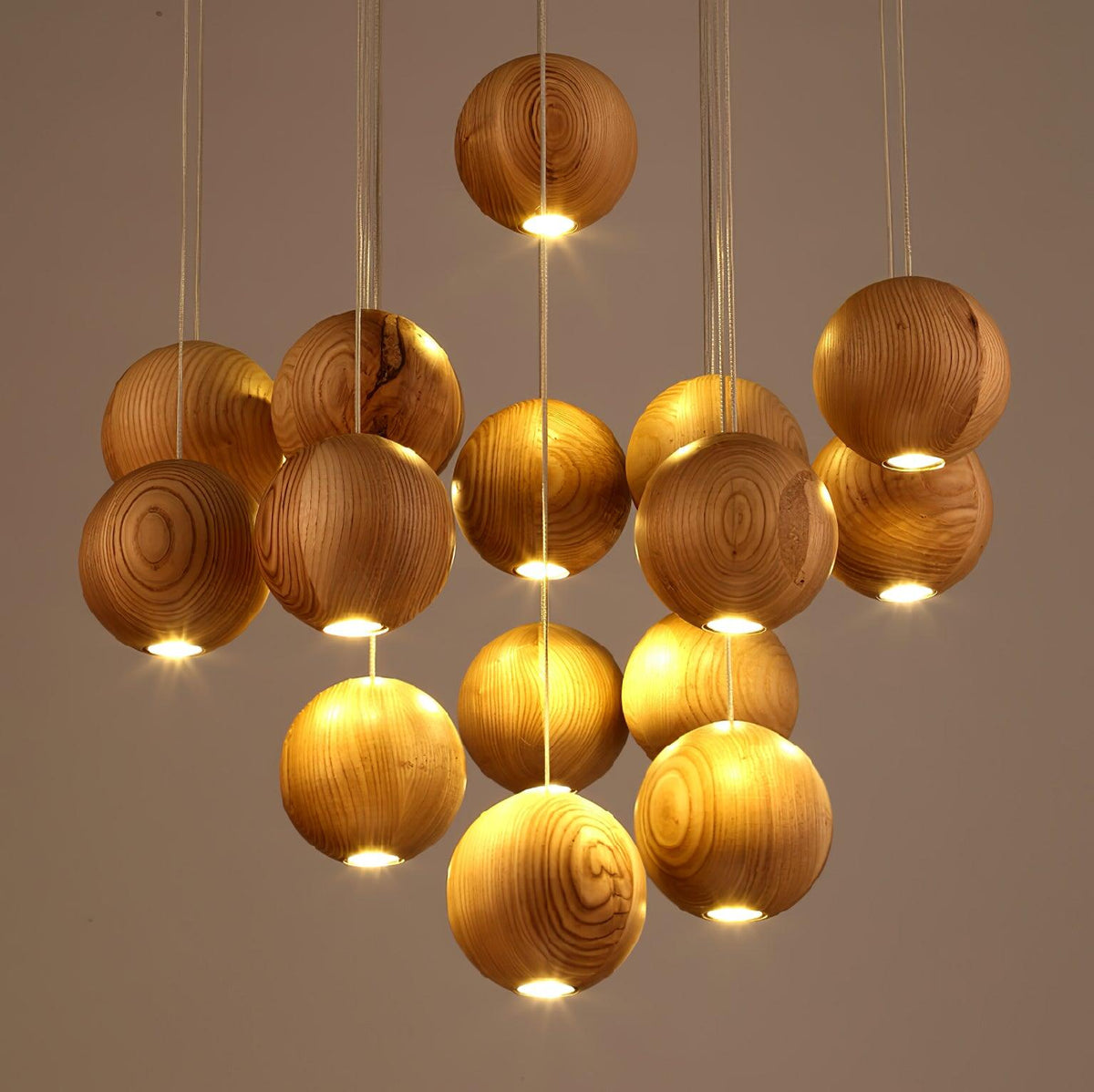 Close view of lit wood spheres on this Clérachic pendant, each with a warm glow from its base, against a soft taupe wall.