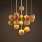 A Clérachic pendant of wood spheres at different heights against a dark brown backdrop, each lit warmly from below.