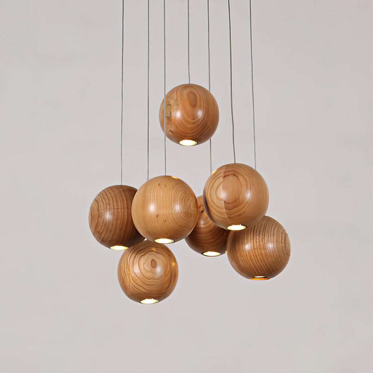 Wood spheres hang at different heights on this Clérachic pendant, each with a small light at its base, against a pale grey backdrop.