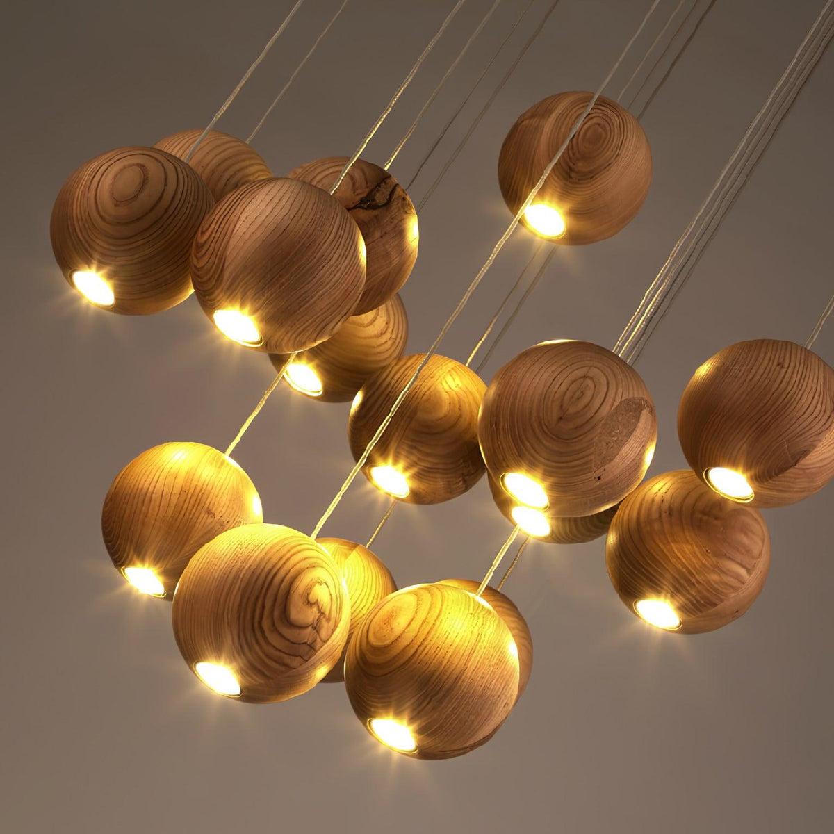 Looking up at the lit wood spheres of this Clérachic pendant, with their cords crossing and a warm light at the base of each.