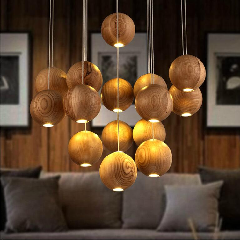A Clérachic pendant of lit wood spheres over a grey sofa, with framed prints on a dark timber wall behind.