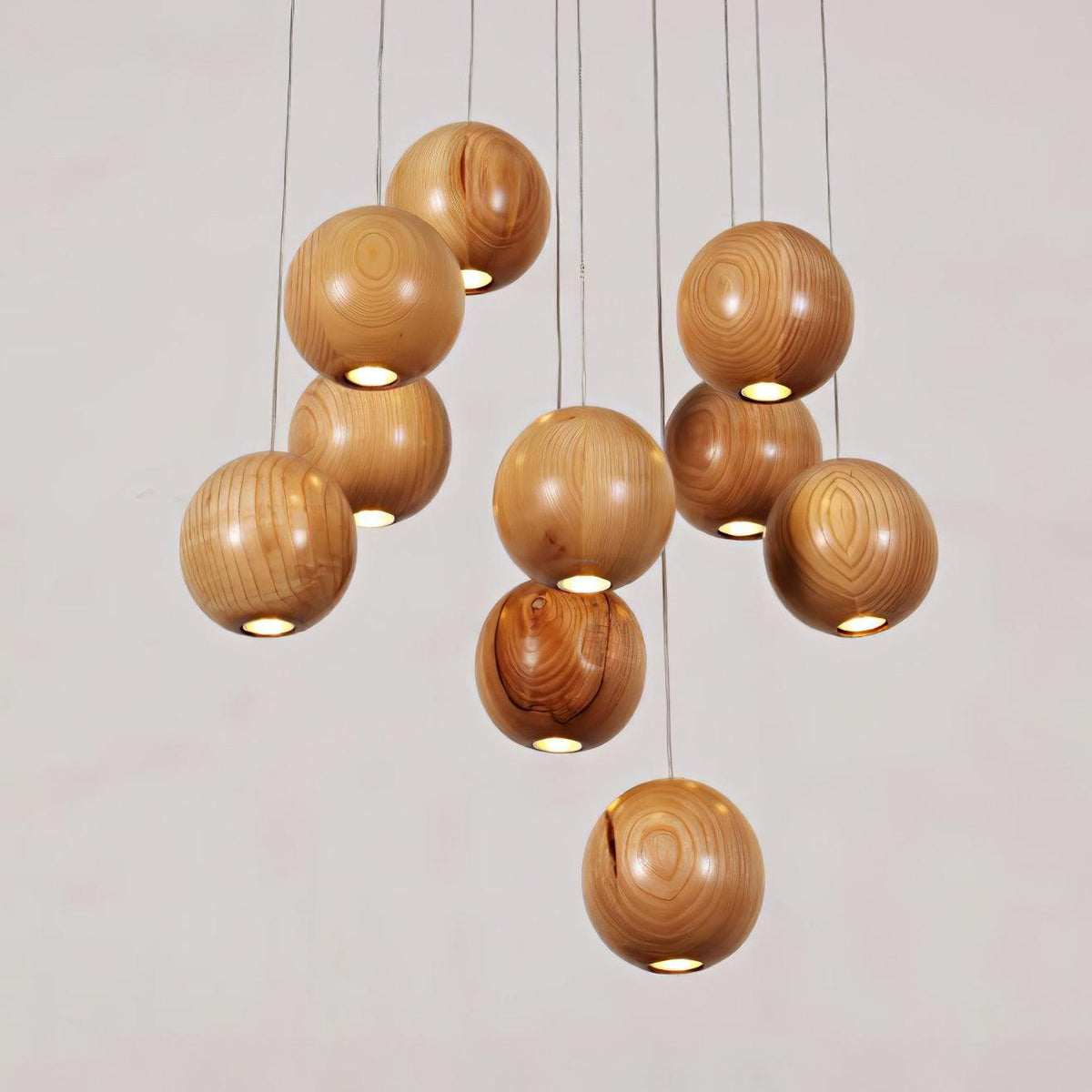 Wood spheres on a Clérachic pendant, each with a small round light opening at the base, against a pale pink-grey wall.